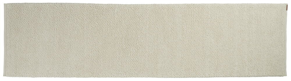 Pitkä valkoinen käsinkudottu matto, jossa on hienovarainen rakenne.