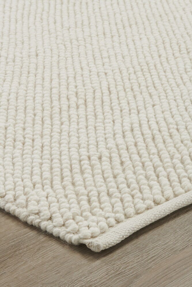 Käsinkudottu luonnonvalkoinen villamatto, jossa on karkea tekstuuri.