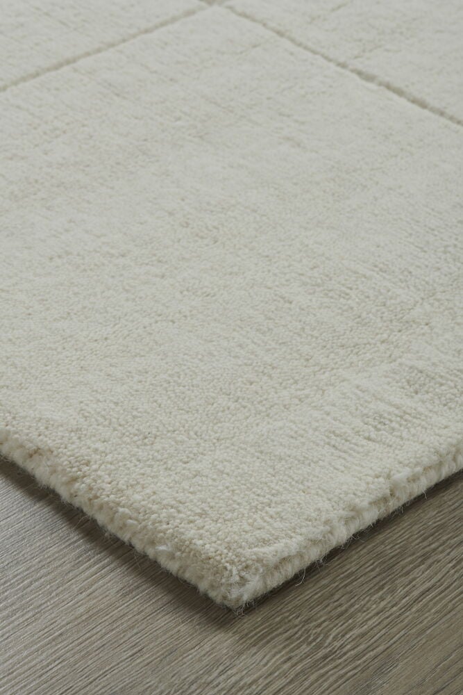 Valkoinen käsinkudottu matto ruutukuviolla lattialla.