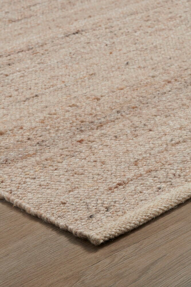 Beige handvävd ullmatta på trägolv.