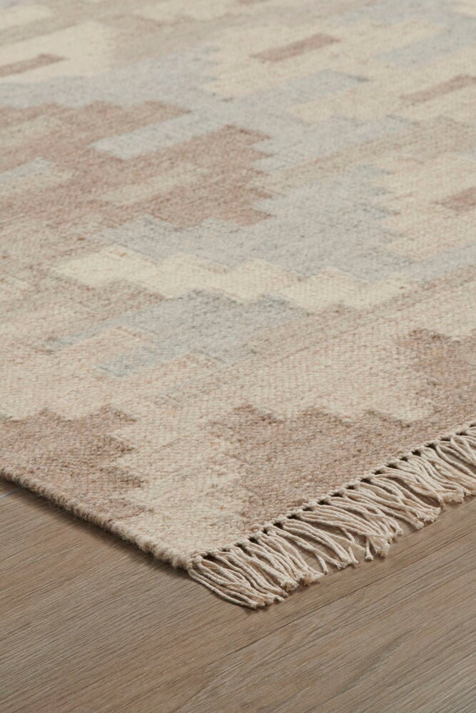 Käsinkudottu villamatto beigeissä sävyissä koristeellisilla hapsuilla.