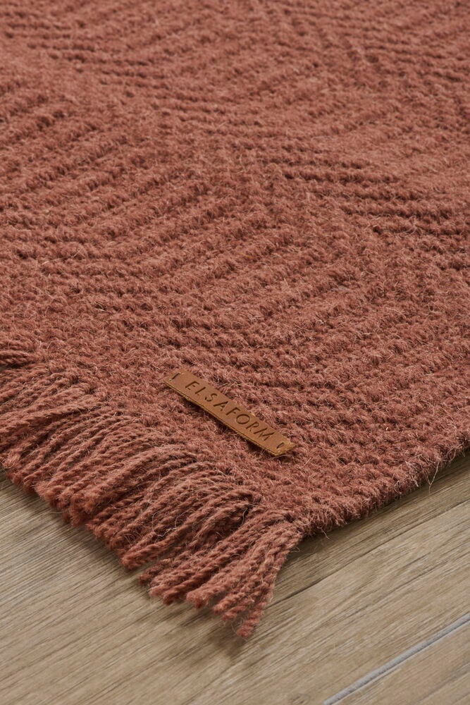 Viininpunaista villakangasta hapsuilla puulattialla.