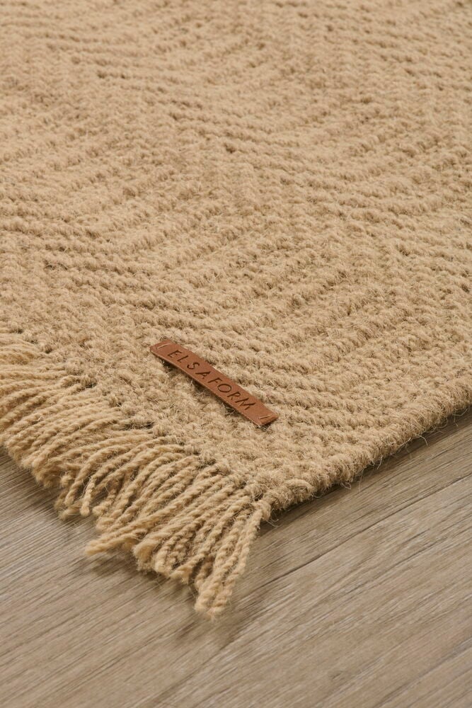 Beige Kamelhaardecke mit Fransen auf Holzboden.
