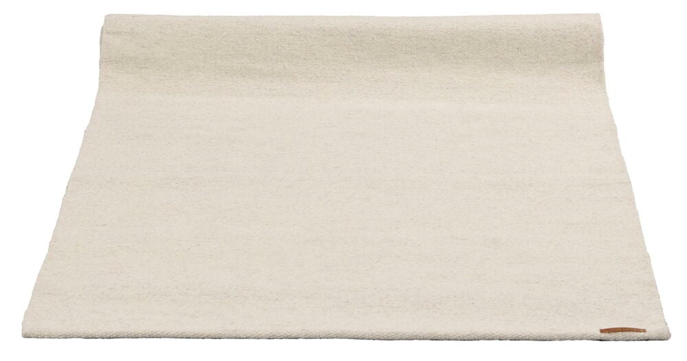 En naturfärgad ullmatta utrullad på golv.