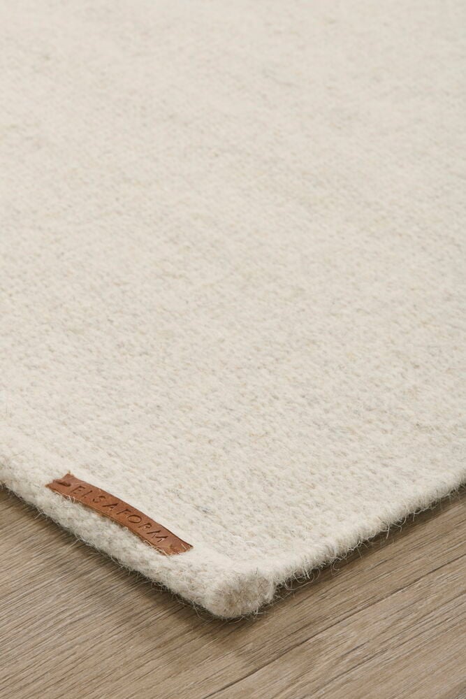 Valkoinen suorakulmainen villamatto puulattialla.