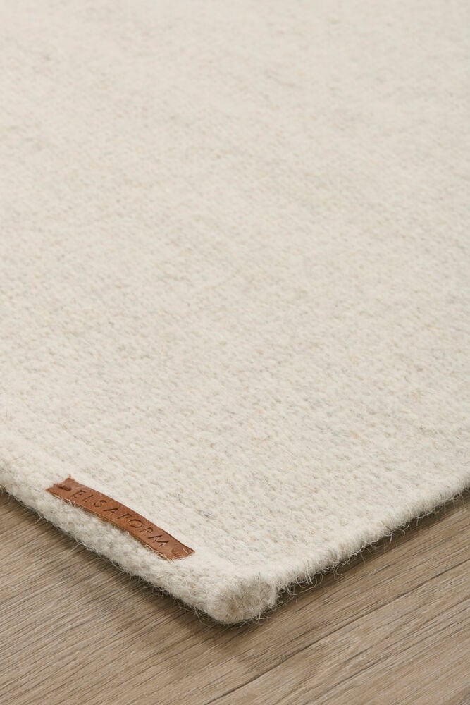 Ljusbeige ullmatta på ljust trägolv.