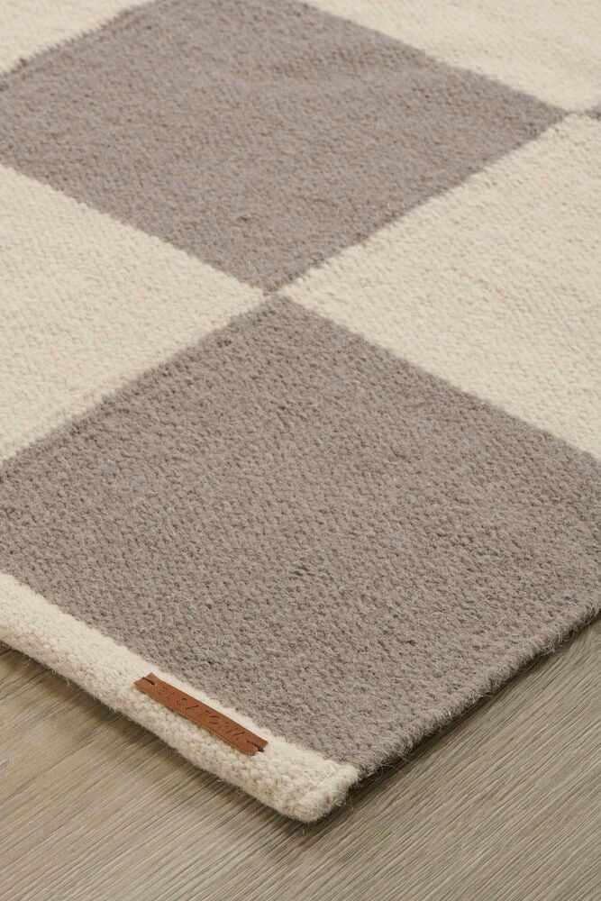 Närbild av en Grå Ullmatta med ljusbeige och grått rutmönster på trägolv.