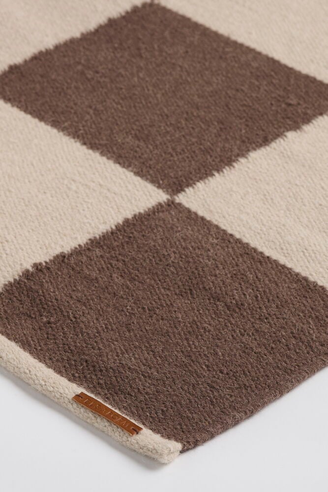 Närbild av en Brun Ullmatta Elsaform Rutan med beige rombmönster och en liten läderlapp.
