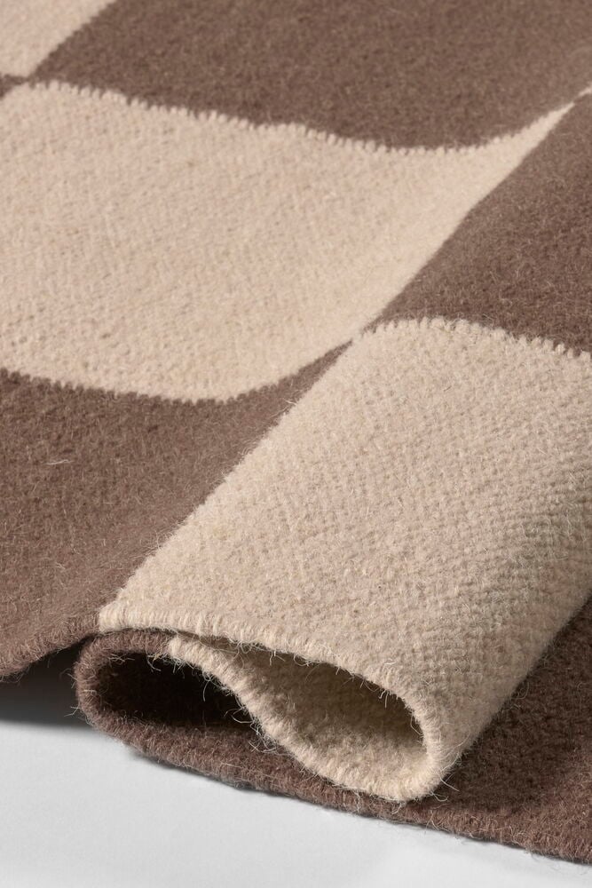 Närbild på en brun och beige Ullmatta Elsaform Rutan med vågigt mönster och mjuk ullstruktur.