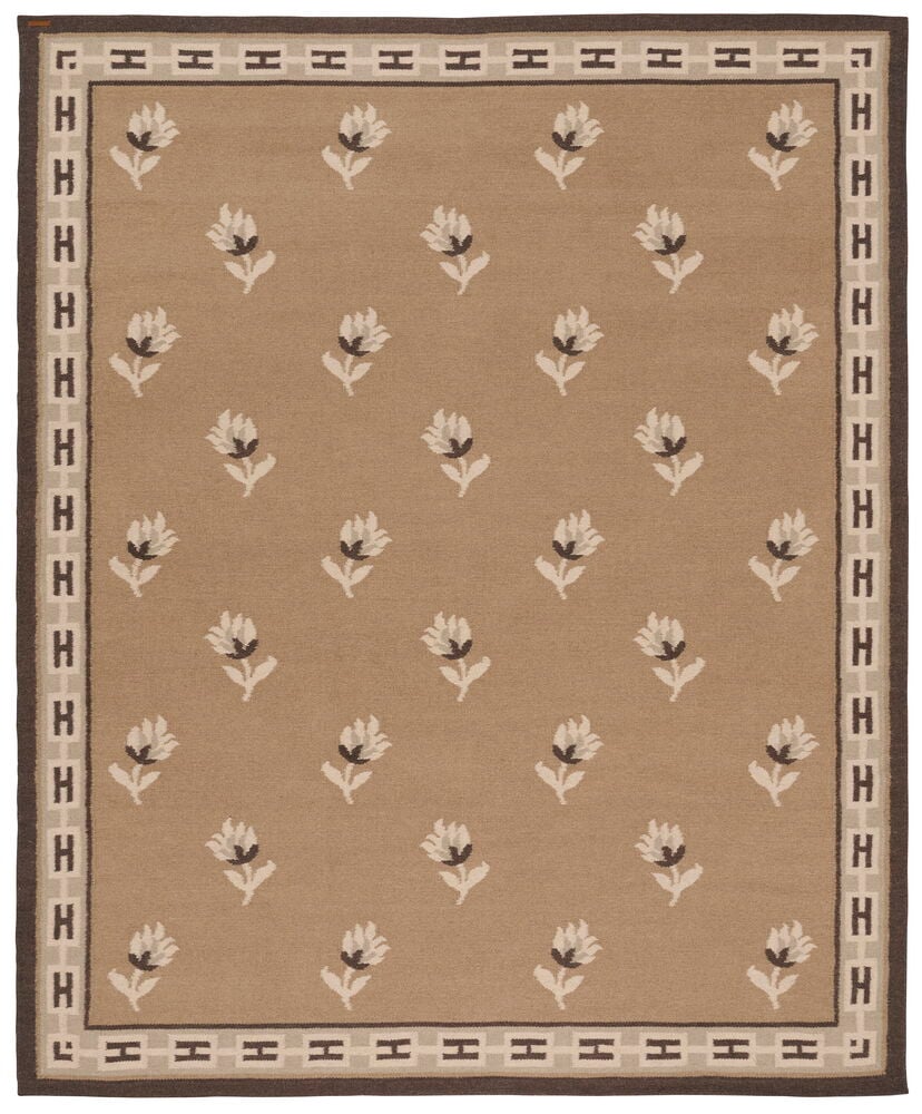 Beige ullmatta med mörk H-mönstrad kant och spridda vita blommotiv.