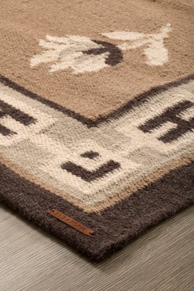 Närbild av en Beige Ullmatta med geometriska och blommiga mönster, med en brun ELSAFORM läderetikett.