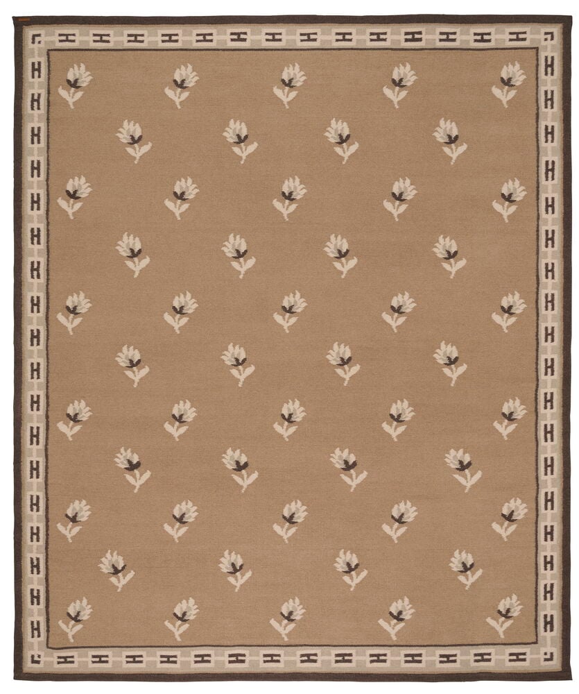En beige ullmatta med ett repeterande vitt och mörkt blommönster och en kant med H-formade motiv.