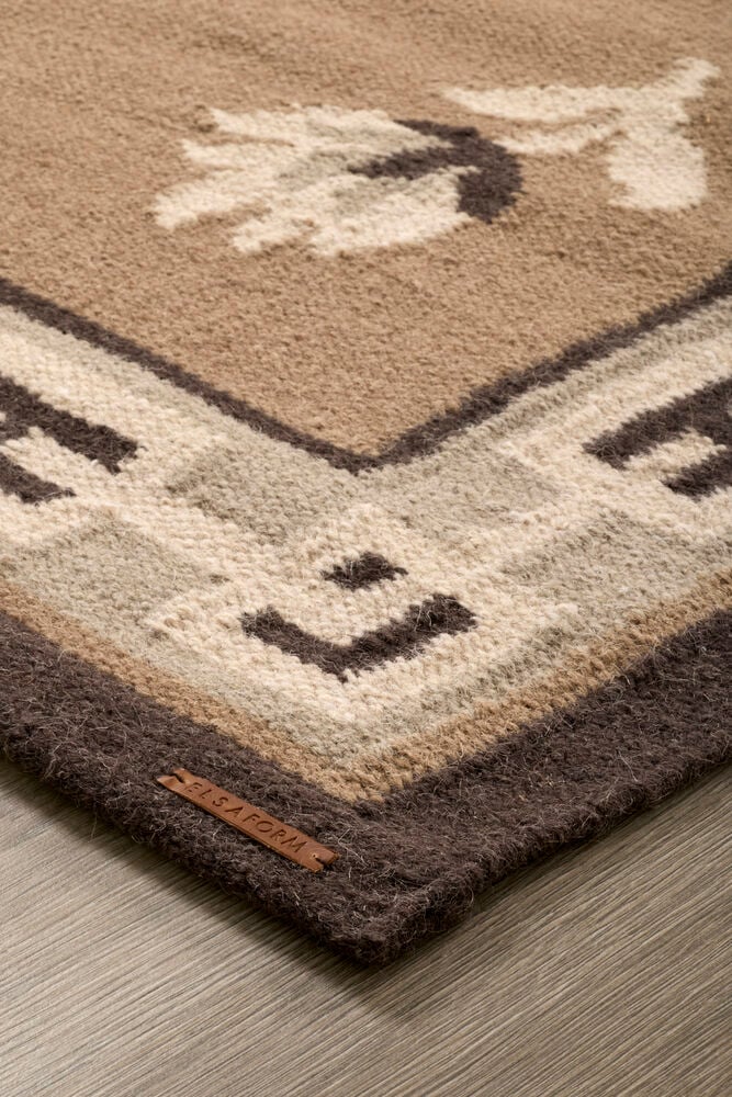 Närbild Beige Ull matta, geometriskt kantmönster i brunt, ljusbeige, benvitt, med en lädertag.