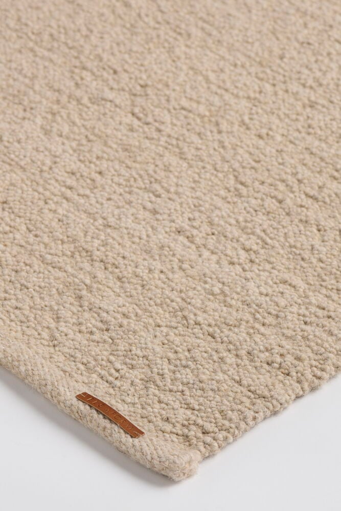 Närbild på en beige matta i ullblandning Elsaform Bonnie med liten brun läderetikett.