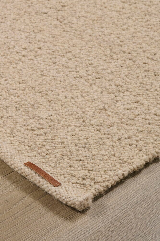 Beige grovvävd matta med en brun läderetikett, visad på ett trägolv.