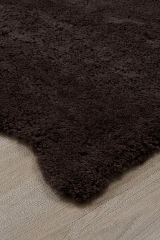 Brunt fårskinn med kort lockigt hår på golv.