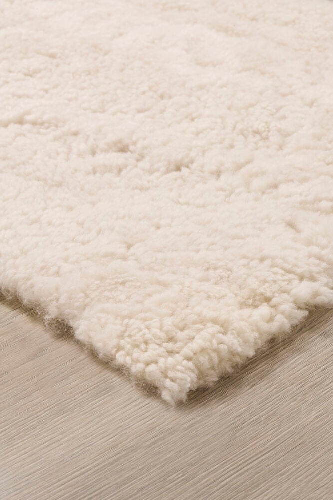 Ljusbeige fårskinnsmatta med kort lockig ull.