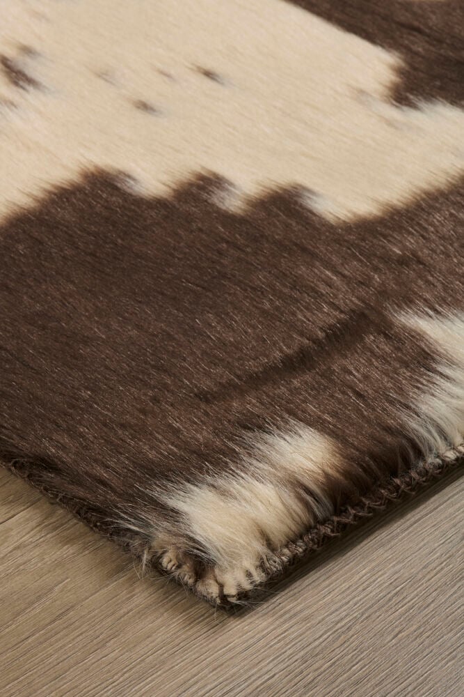 Brun og kremfarget polyester fuskepels teppe med ku-skinnmønster.