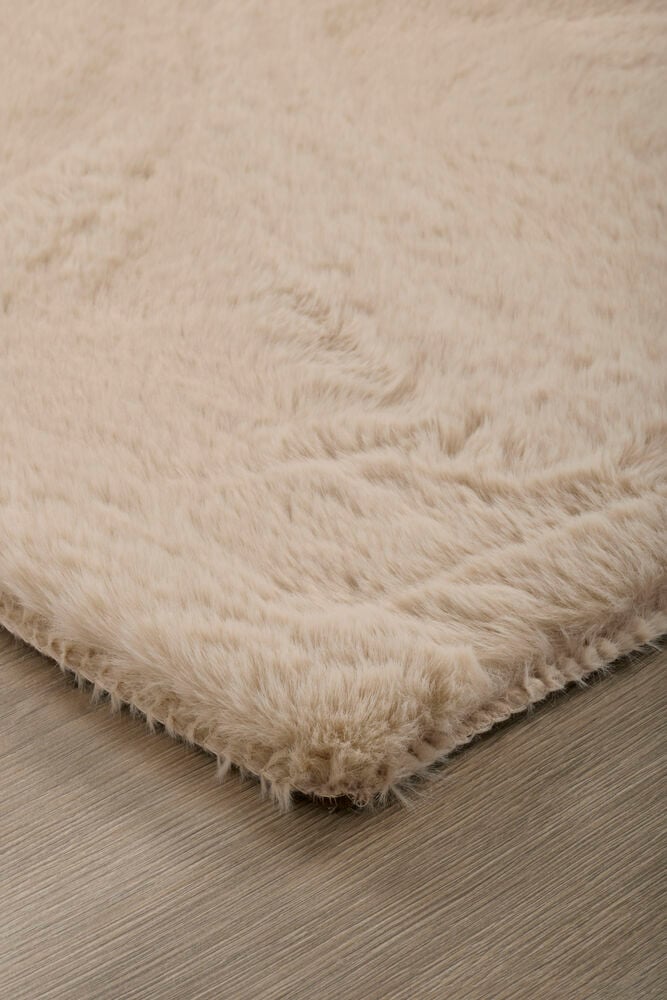 Nærbilde av en Beige Polyester fuskepelsmatte med myk lugg, plassert på et lyst tregulv.