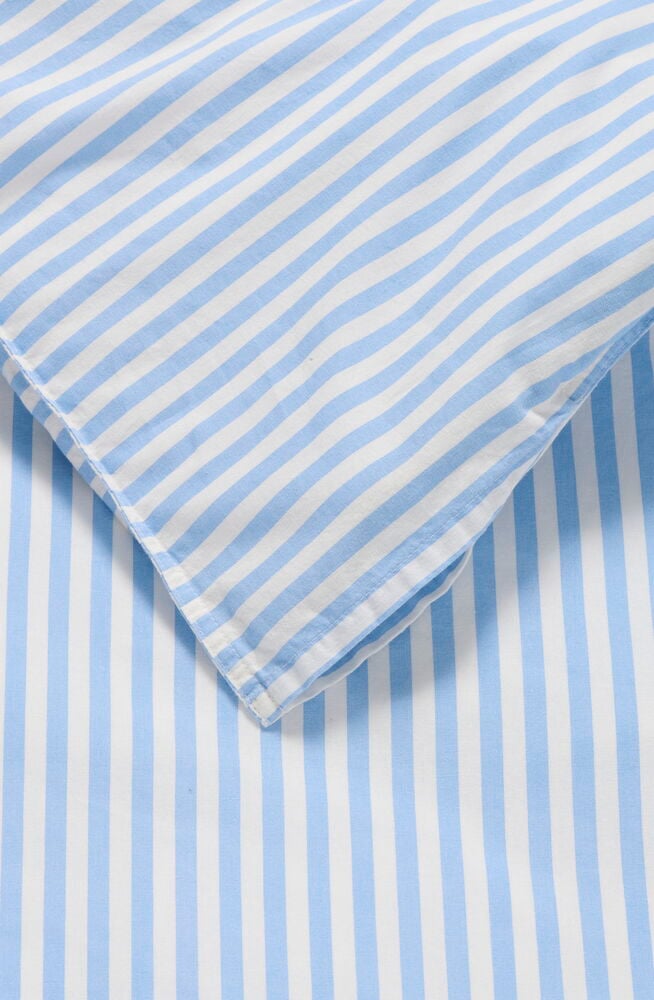 Nahaufnahme eines hellblau-weiß gestreiften Vida Bettwäsche-Sets aus Baumwolle mit einer gefalteten Ecke.