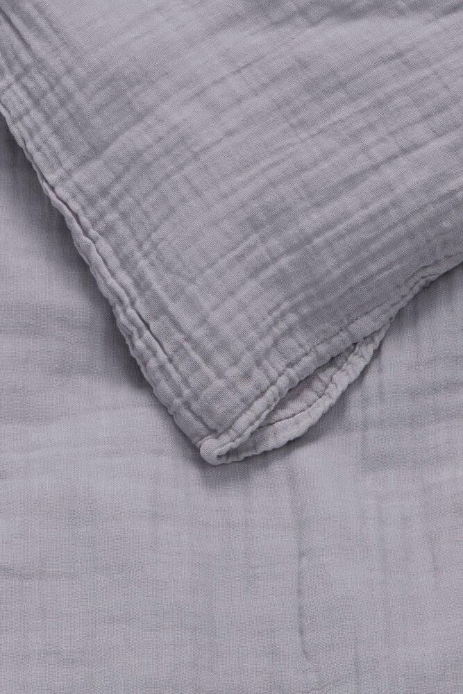 Grått muslin påslakanset med kuddfodral och täcke.