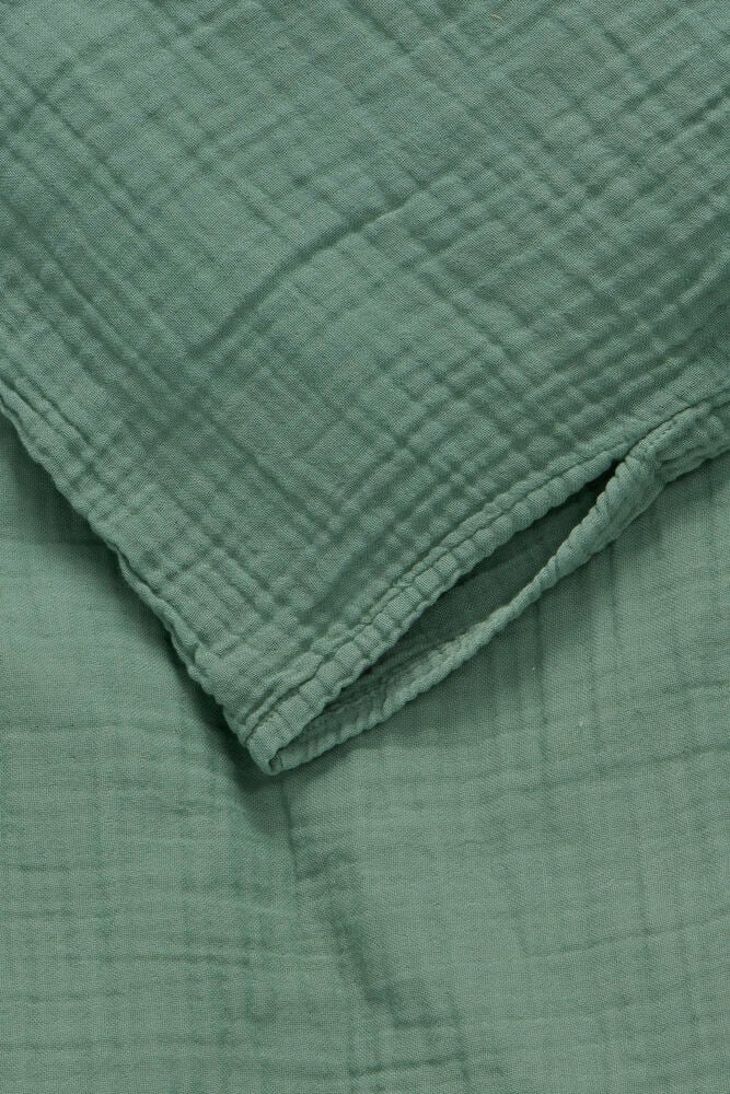 Ein grünes Bettwäsche-Set aus Musselin-Baumwolle, gefaltet mit knitteriger Textur, Nahaufnahme.