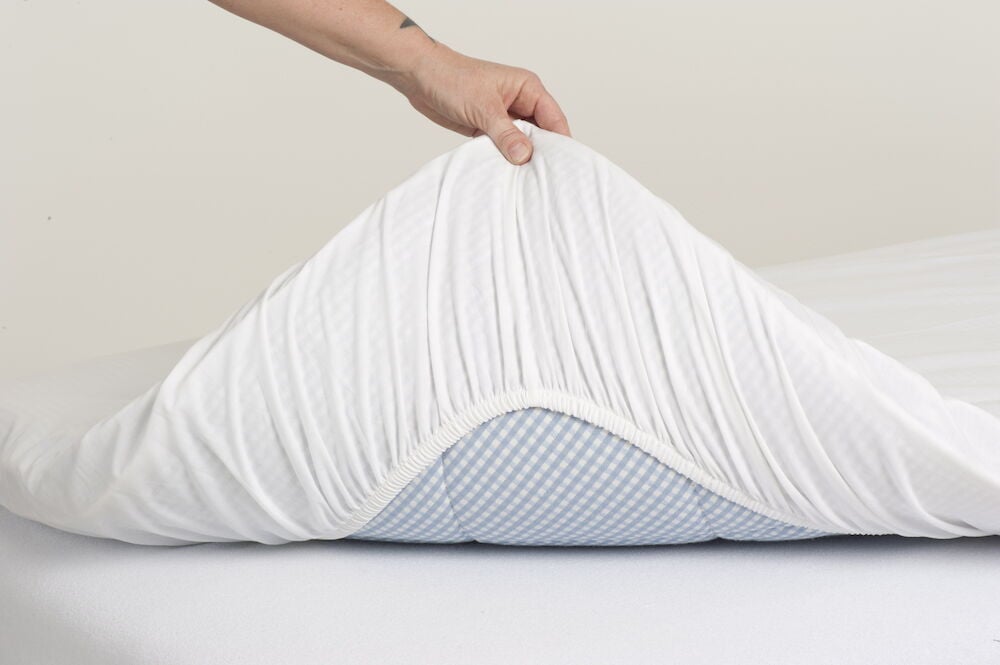 Käsi asettaa valkoisen vedettävän lakanan patjalle.