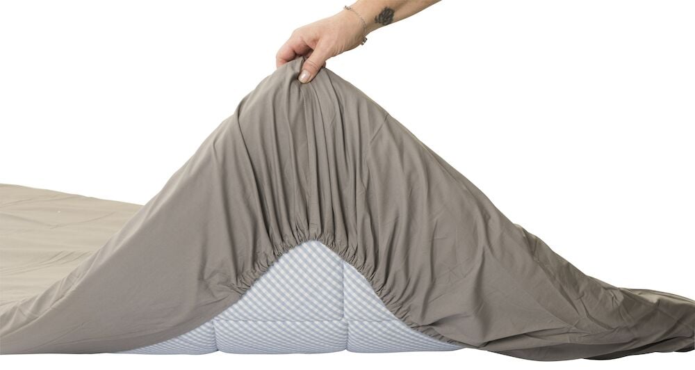Harmaa puuvillainen aluslakana vedetään patjan päälle.