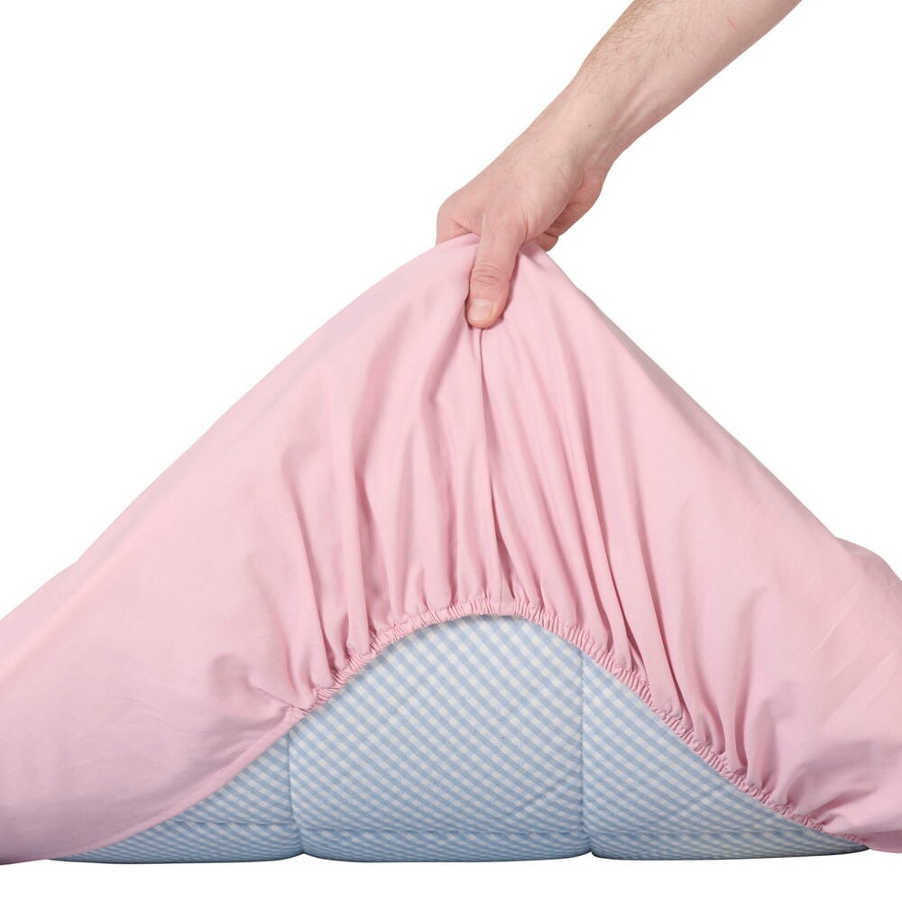 Ett gammelrosa dra-på-lakan dras över madrass.