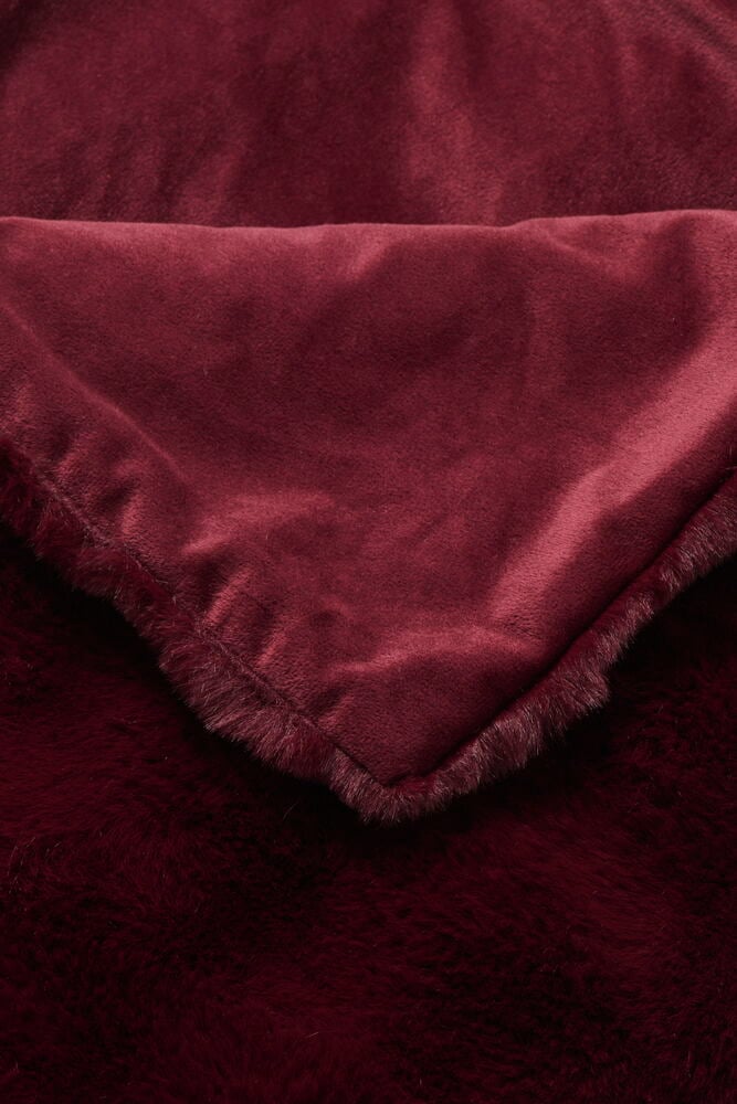 En vikt gammalvinröd Polyester Pläd Fluff visar sin mjuka fluffiga textur och släta baksida.