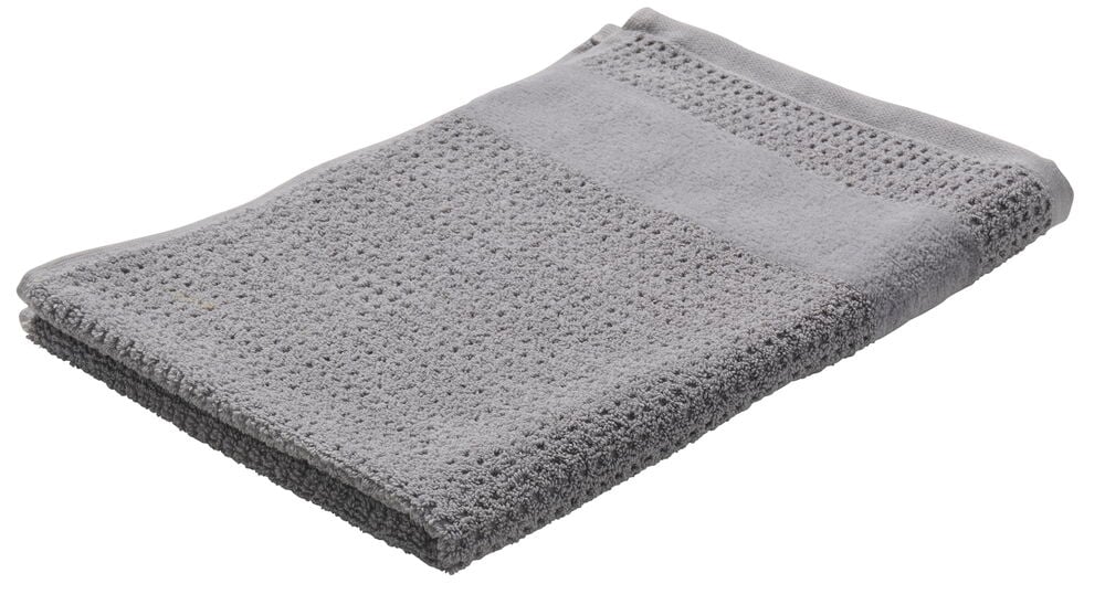 En vikt grå handduk i bomull på vitt underlag.