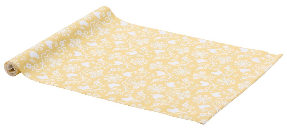 Keltainen pöytäliina, jossa on valkoinen lintu- ja lehtikuvio.