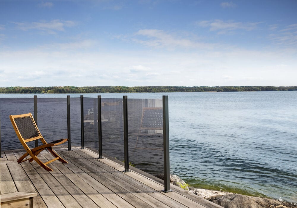 Harmaat alumiinipylväät puuterassilla järven rannalla.