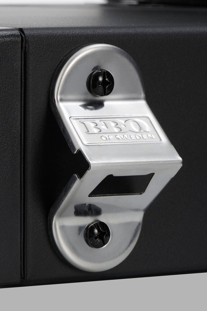 Silberner Flaschenöffner mit 'BBQ OF SWEDEN'-Prägung, an einem schwarzen Propangasgrill Forge mit Schrauben befestigt.