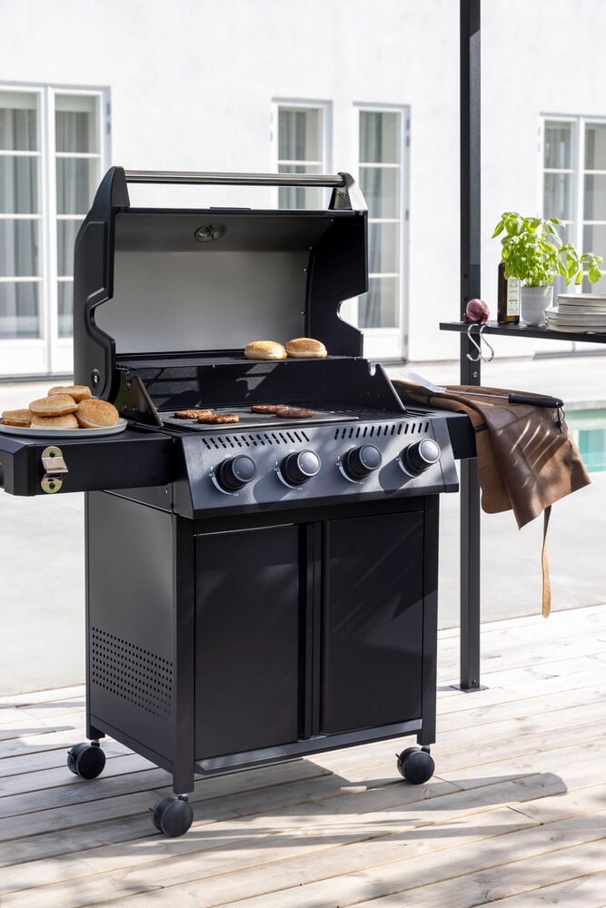 Schwarzer Propangasgrill Titan mit offenem Deckel, der Burger und Brötchen grillt, und eine braune Lederschürze.