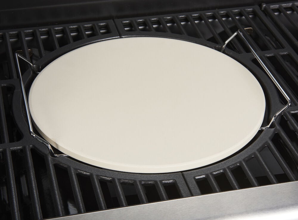 Rund pizzastein i keramikk på svart grillrist.