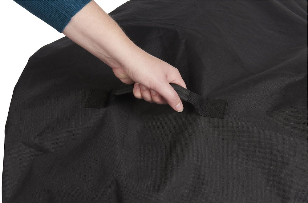 Käsi nostaa mustan grillisuojuksen kiinnitysremmillä.