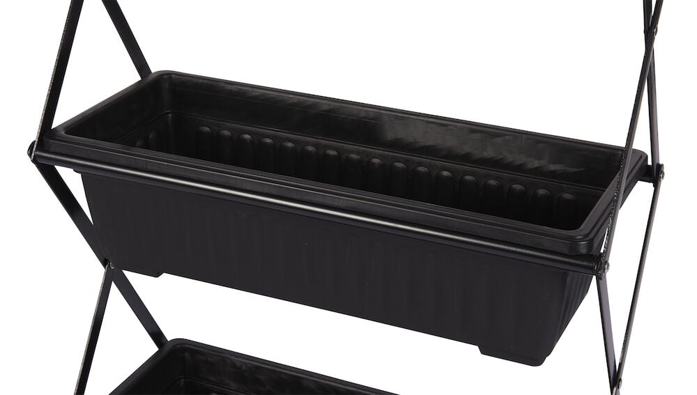 Svart rektangulär blomlåda på växthylla av metall.