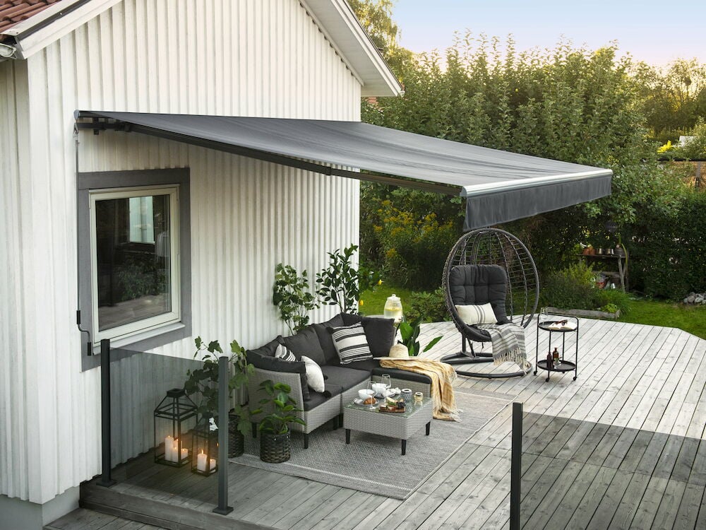 Grå terrassmarkis monterad över uteplats med utemöbler.
