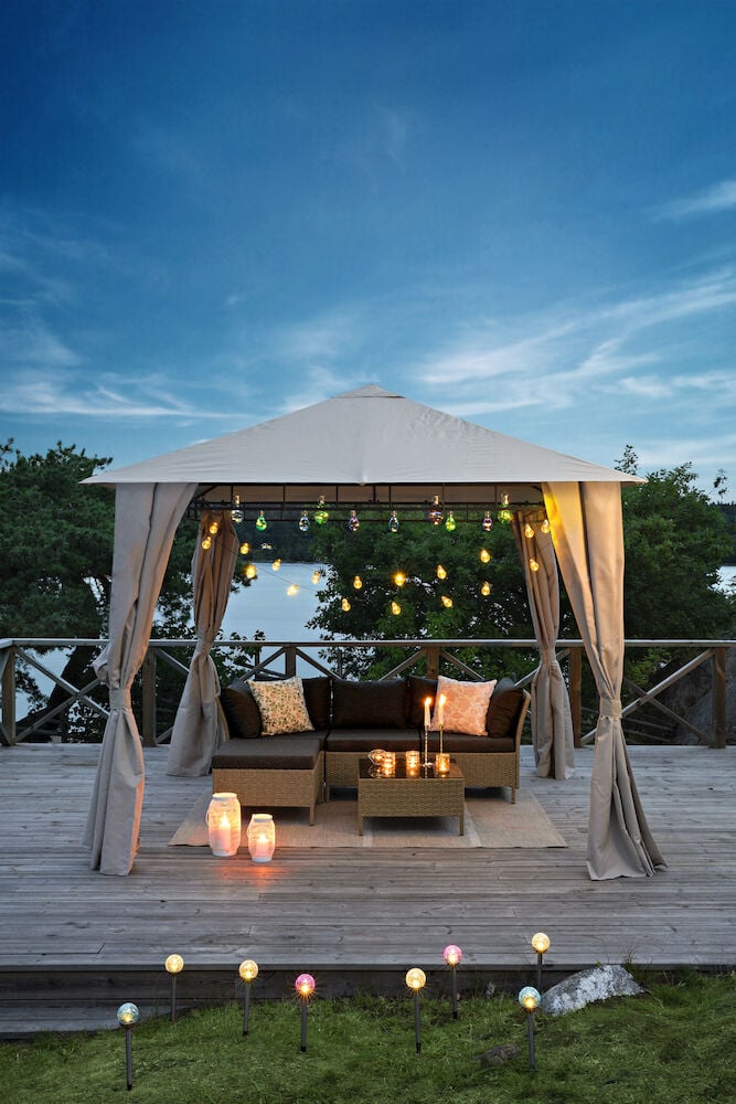 Paviljong med gardiner og møbler på en treterrasse.