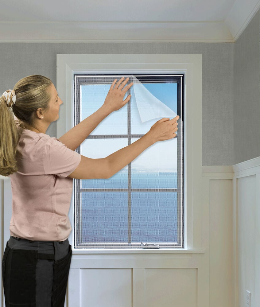 Frau montiert weißes Insektennetz am Fenster.