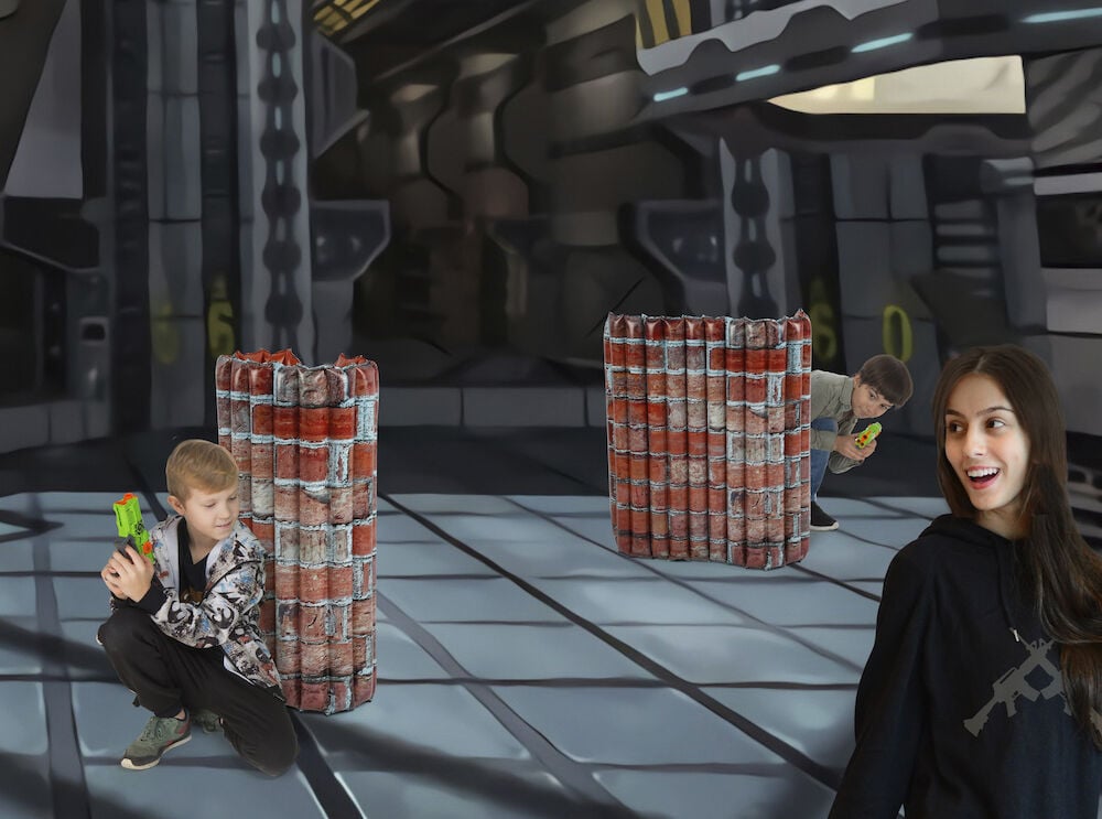 Två Uppblåsbar leksak Battle zone Brick wall 96x6x86 cm. Pojkar håller blasters; en kvinna bär svart hoodie med gevärstryck.