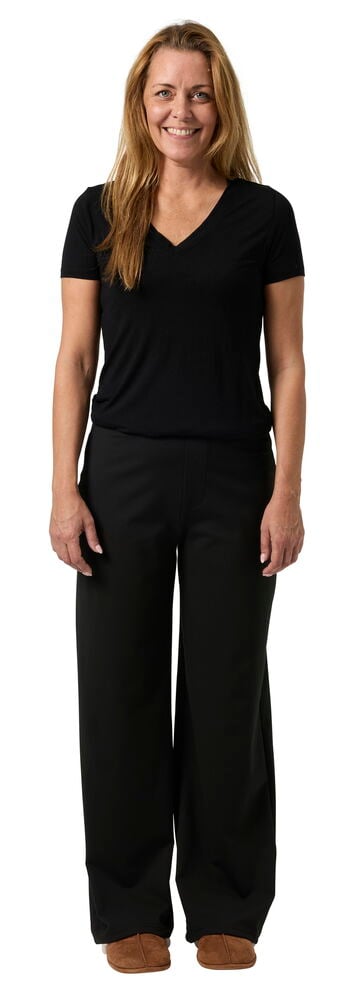 Ganzkörperansicht von vorne einer Frau in schwarzer Wide Hose, schwarzem V-Ausschnitt-T-Shirt und braunen Hausschuhen.