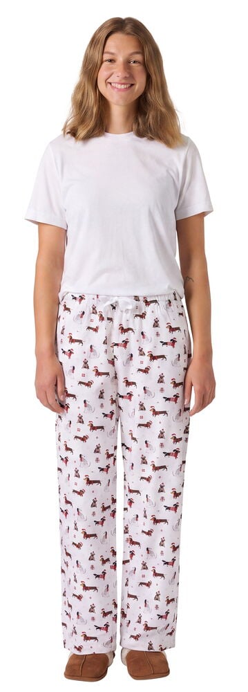 Kvinna bär vita Pyjamasbyxor Flannel Santa Santa Dogs Bomull, en vit t-shirt och bruna tofflor, framifrån.