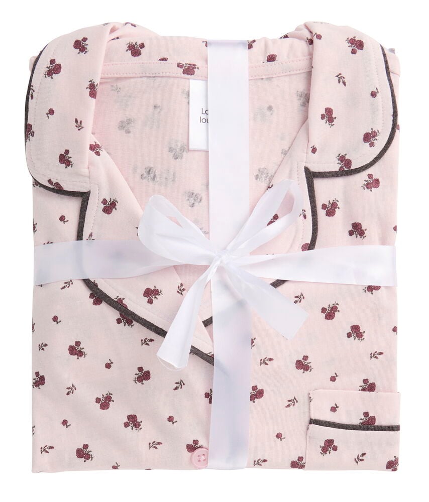 Taitettu vaaleanpunainen kukkakuvioinen Pyjama Klara, jossa tummanruskea reunus, näkyvä nappi ja valkoinen rusetinauha.