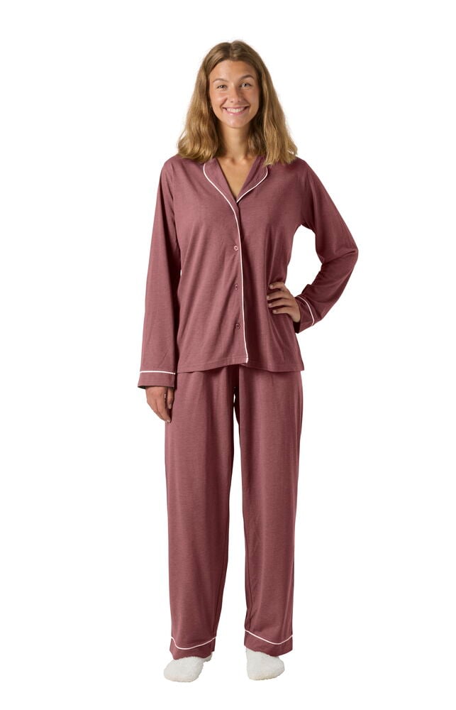 Nainen yllään ruusunpunainen Pyjama Laura pitkähihainen paita, yhteensopivat housut valkoisella tereellä ja valkoiset tossut.