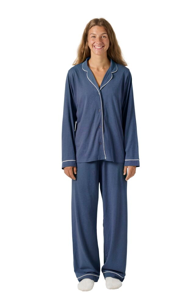 Nainen sinisessä Pyjama Laura setissä: pitkähihainen paita, housut valkoisella tereellä ja valkoiset tossut.