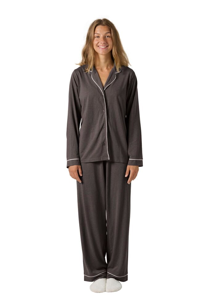 Nainen pukeutuu tummanharmaaseen Pyjama Laura -settiin valkoisilla reunuksilla ja valkoisiin tossuihin, edestä.