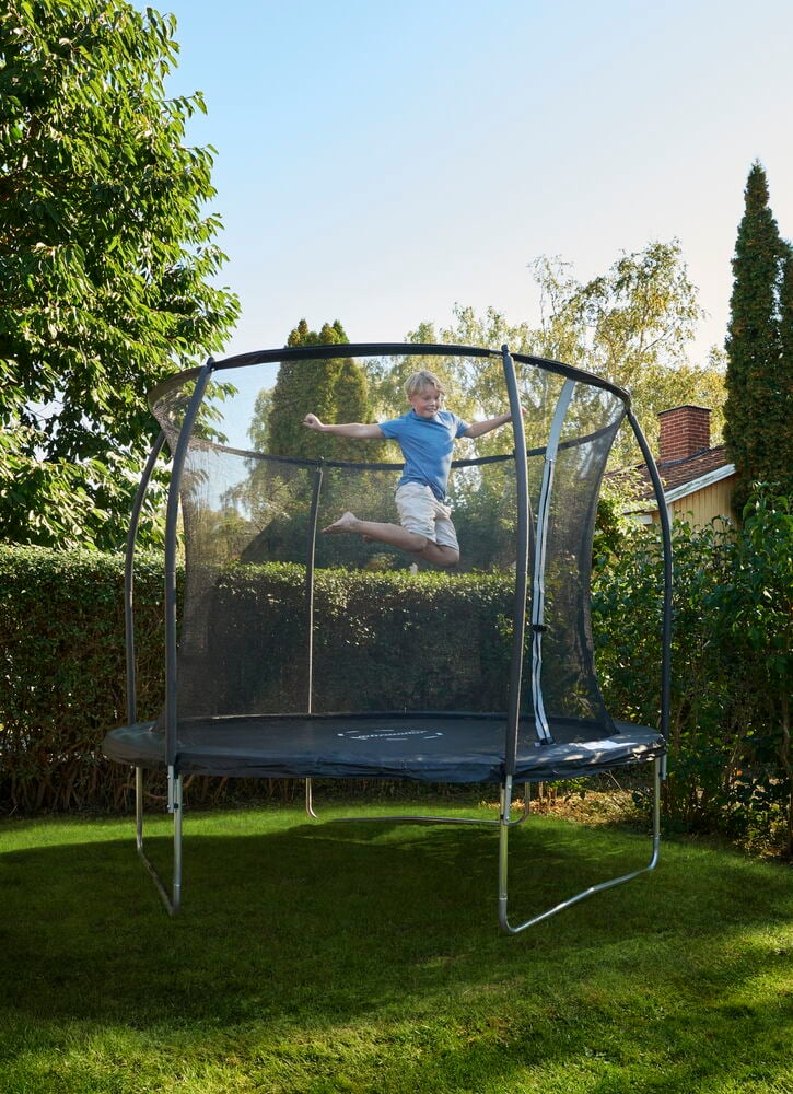Barn hopper på trampoline med sikkerhetsnett utendørs.