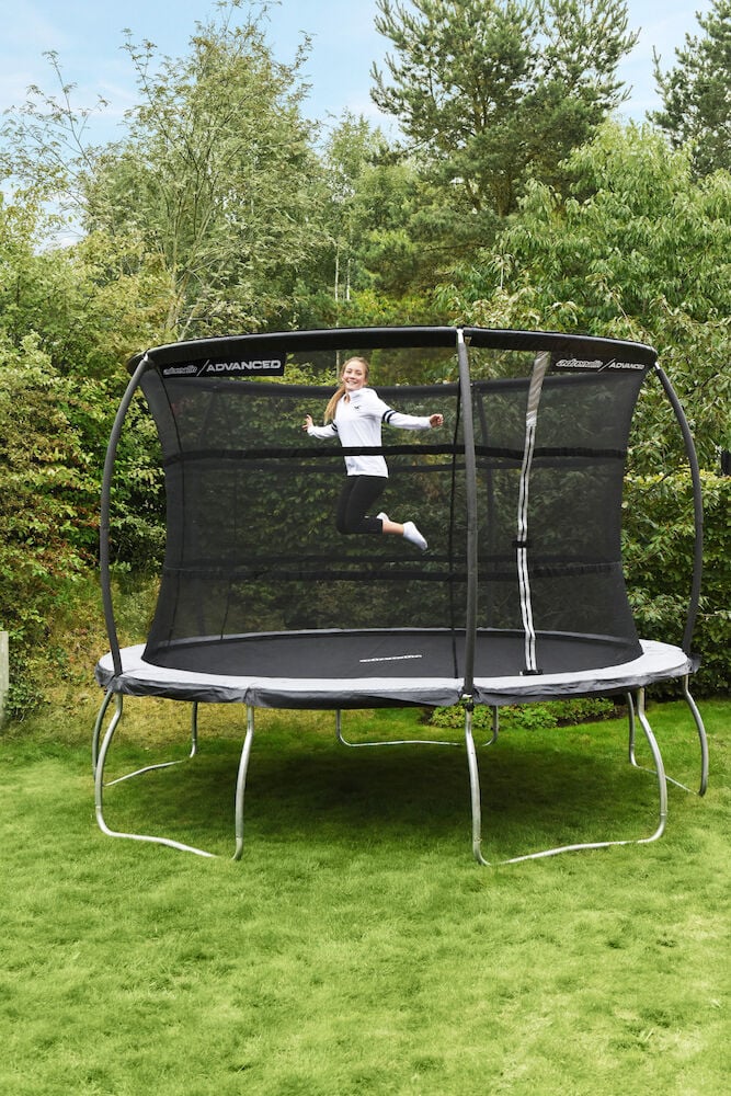 Trampoliini turvaverkolla ja pomppivia lapsia ulkona.